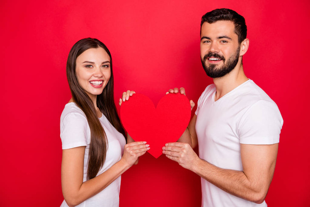 Photo of lovely nice cute charming couple of two people together holding heart with their hands wearing white t-shirt while isolated with red background - Foto, imagen