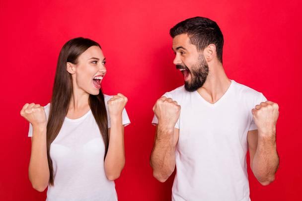 Photo of cheerful charming cute fascinating trendy stylish handsome beautiful couple of two people rejoicing with victory of something while wearing white t-shirts isolated with red background - Photo, image