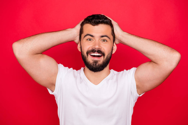 Close up photo of cheerful rejoicing enjoying guy having known some excellent news with his hands holding head while isolated over red background - Foto, imagen