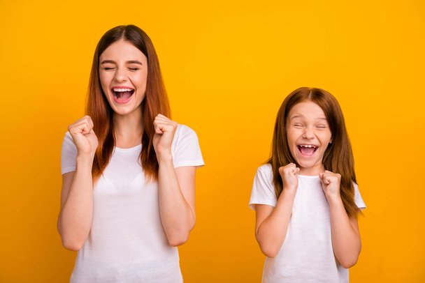 Portrait of cheerful crazy people with long hair screaming raising fists wearing white t-shirt isolated over yellow background - Фото, зображення