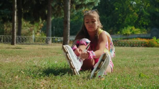 Young girl putting on her rollerblades sitting on grass - Záběry, video