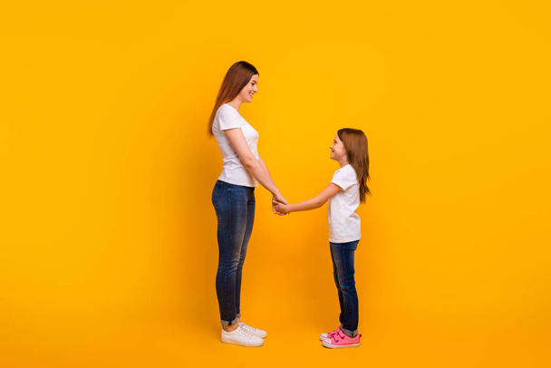 Full length profile side photo of lovely mommy with her kid having long haircut holding hands isolated over yellow background - Fotoğraf, Görsel