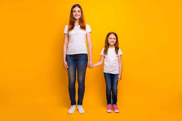 Full size photo of cheerful ladies holding hand smiling wearing white t-shirt denim jeans isolated over yellow background - Фото, зображення
