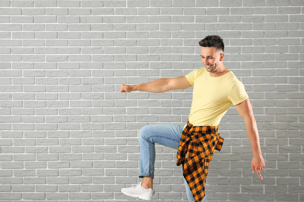 Handsome young man dancing against brick wall - Photo, Image