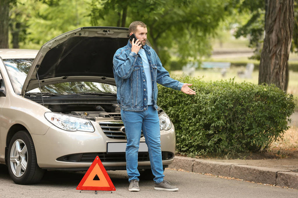 Man calling his insurance agent while standing near broken car on road - Photo, Image