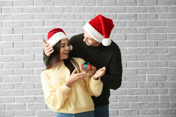 Człowiek dając swoją dziewczynę prezent świąteczny przeciwko ścianie cegły - Zdjęcie, obraz