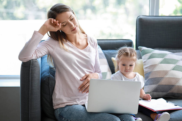 Tired pregnant businesswoman with daughter working at home - Φωτογραφία, εικόνα