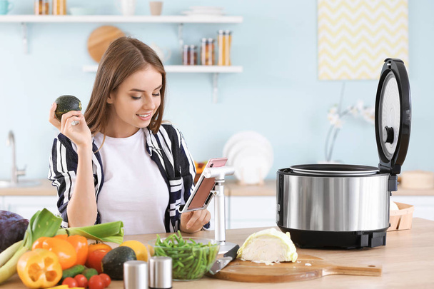 Femme utilisant téléphone portable et cuisinière multi dans la cuisine
 - Photo, image