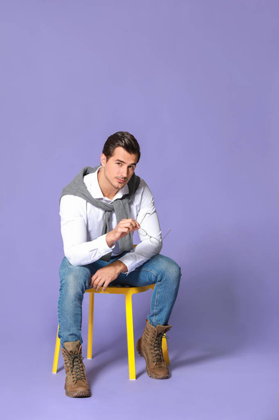 Fashionable man sitting on chair against color background - Valokuva, kuva
