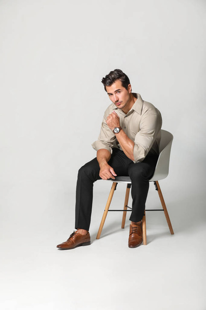 Fashionable man sitting on chair against light background - Foto, Imagen