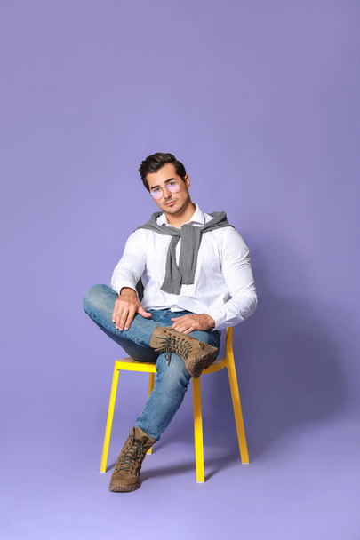Fashionable man sitting on chair against color background - Foto, Bild