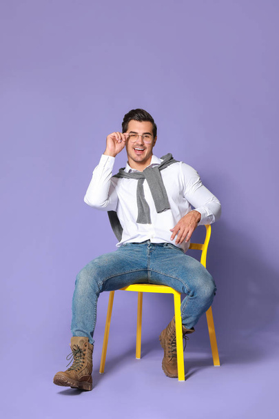 Fashionable man sitting on chair against color background - Foto, immagini