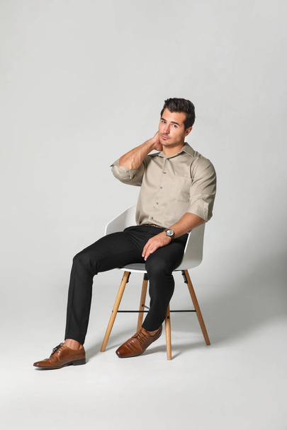 Fashionable man sitting on chair against light background - Photo, Image