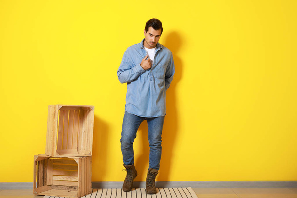 Stylish fashionable man and wooden boxes against color wall - Photo, Image