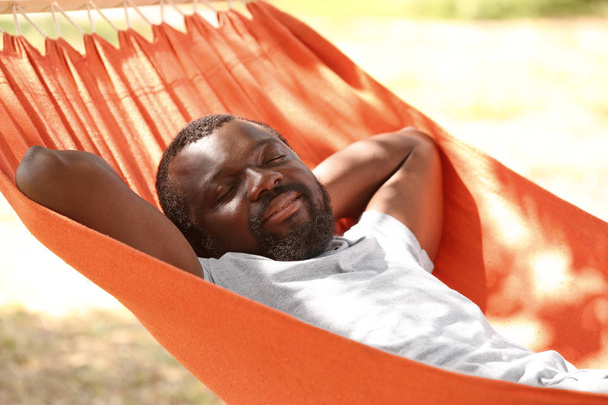 Afro-Amerikaanse man ontspannen in hangmat buitenshuis - Foto, afbeelding