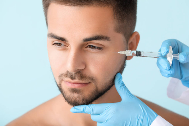 Handsome man receiving filler injection on color background - Фото, зображення