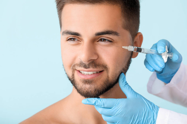 Handsome man receiving filler injection on color background - Foto, imagen