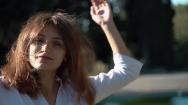 Beautiful girl close-up. Girl posing for the camera in a white shirt in the park. Lush hair.  - Materiał filmowy, wideo