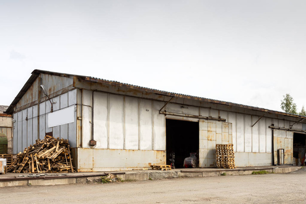 Um grande armazém industrial de metal para armazenar mercadorias, ao lado dele são paletes de madeira para armazenar mercadorias. Conceito industrial de transporte, carga e armazenamento de mercadorias
 - Foto, Imagem