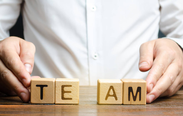 A businessman joins together two parts of the word Team. personnel management, the organization and creation of working groups and teams, the creation of links between individual teams and departments - Valokuva, kuva