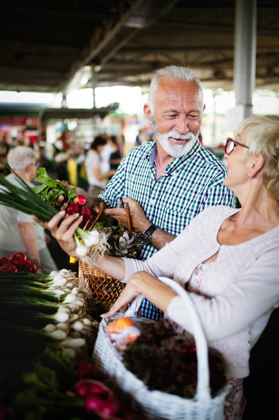 Smiling senior couple holding basket with vegetables at the grocery shop - Foto, immagini
