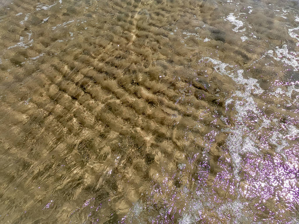 The texture of clear water with sandy bottom. Wave on the seashore or ocean. - Foto, afbeelding