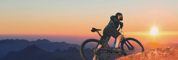 Conquistar picos de montaña por ciclista en pantalones cortos y jersey en una moderna bicicleta rígida de carbono con una horquilla de suspensión neumática. Hermosa vista desde la montaña. Vista panorámica de la pancarta. - Foto, imagen