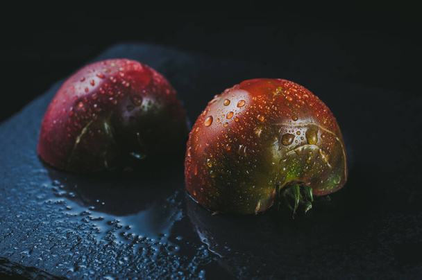 Домашние красивые нарезанные красные мокрые помидоры в капли на черном sto
 - Фото, изображение