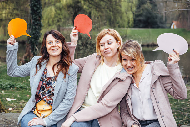 Gruppe von Mädchen im Park mit seltsamen Gesichtsausdrücken, während sie eine Gedankenblase auf ihren Händen halten. Freundschafts- und Kommunikationskonzept. - Foto, Bild