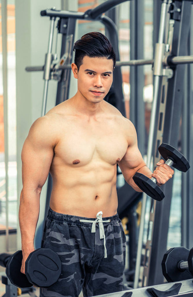 Muscular man bodybuilder training with dumbbells. - Foto, Bild