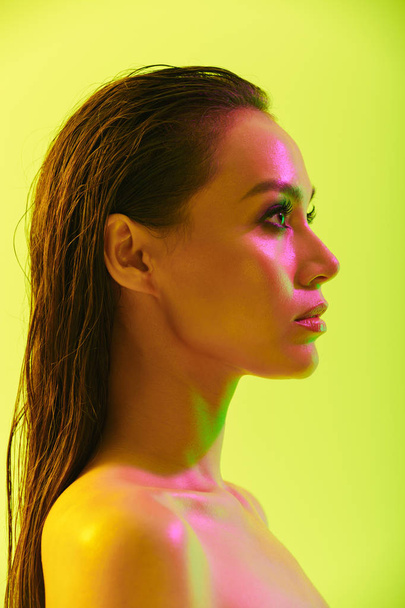 Beautiful young woman posing isolated over yellow wall background with neon bright lights. - Fotó, kép