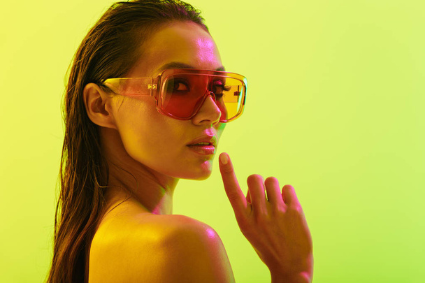 Amazing young woman posing isolated over yellow wall background with neon bright lights wearing fashion sunglasses. - Foto, immagini