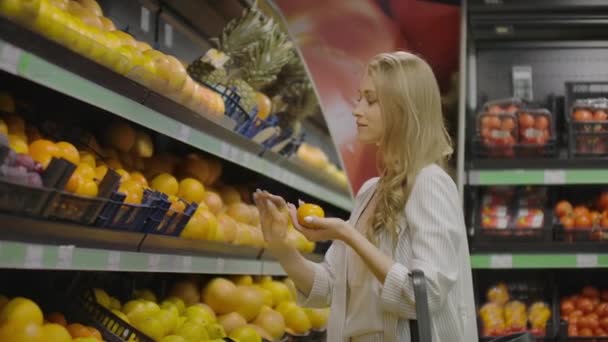 Slow motion girl chooses tangerines puts into bag. Slow motion close view girl hand chooses fresh aromatic tangerines and put into plastic bag against boxes. - Filmmaterial, Video