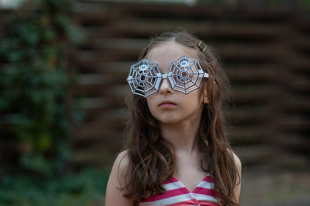 9-10歳の女の子は、ハロウィーンや夏のテーマパーティーのためのクモのデザインのメガネを着ていた. - 写真・画像