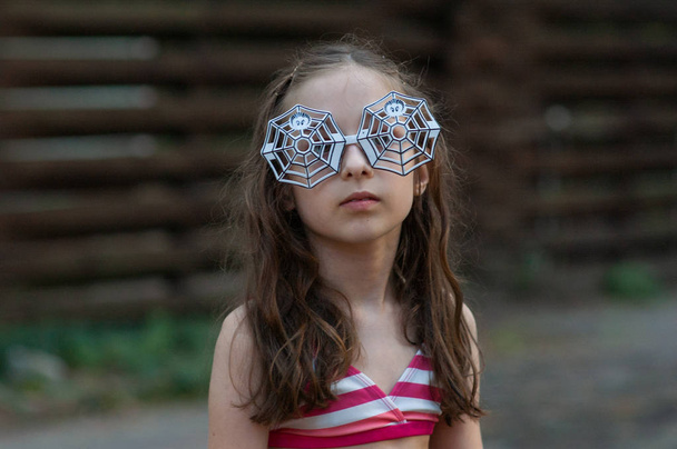 ein Mädchen im Alter von 9-10 Jahren trug eine Brille mit Spinnenmuster für Halloween oder eine sommerliche Themenparty. - Foto, Bild