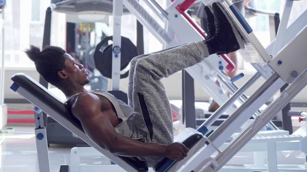 Muscular africano fitness hombre haciendo ejercicio en la máquina de prensa de piernas en el gimnasio
 - Foto, imagen