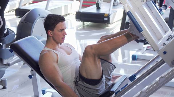 Yakışıklı genç yırtık erkek atlet bacak pres makinesi üzerinde egzersiz - Fotoğraf, Görsel