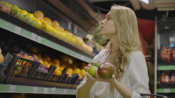 Mladá žena si vybírá zralý manga v obchodě. Vegan nulová odpadová dívka nakupující ovoce a vegetariánské produkty v Biosupermarketu a použití sáčku na znovupoužití. 4k pomalý pohyb. - Záběry, video