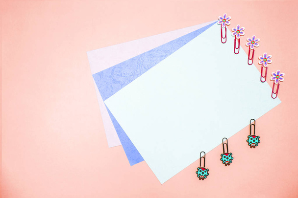 Office: pink copyspace background, several sheets of cardboard, and beautiful paper clips in the shape of daisies and ladybugs matte colors. - Photo, Image