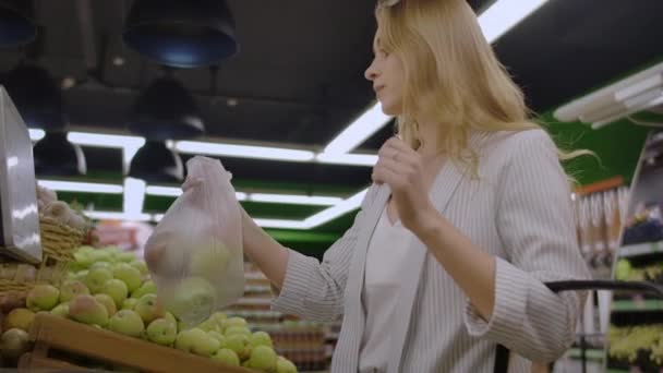 Mujer joven pesando manzanas en la balanza electrónica. Ama de casa Compras en un supermercado en el Departamento de Frutas y Verduras. A cámara lenta. Concepto Venta, Compras, Consumismo y Gente
. - Imágenes, Vídeo