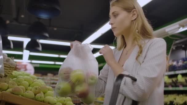 Middle-aged woman weighs a bag of apples in the supermarket. - Video