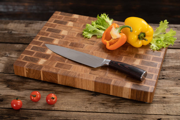 Red, ripe, bright tomatoes and peppers lie on a wooden cutting board near the kitchen knife. - Photo, image