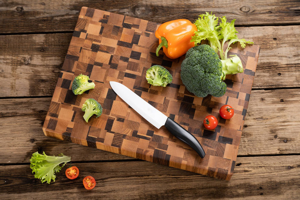 Bright tomatoes and peppers lie on a wooden cutting board near the kitchen knife. - Foto, immagini