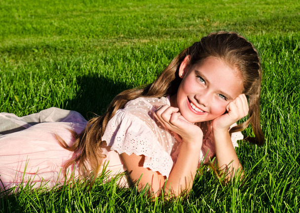 Adorable happy little girl child lying on the grass in the park  - Фото, изображение