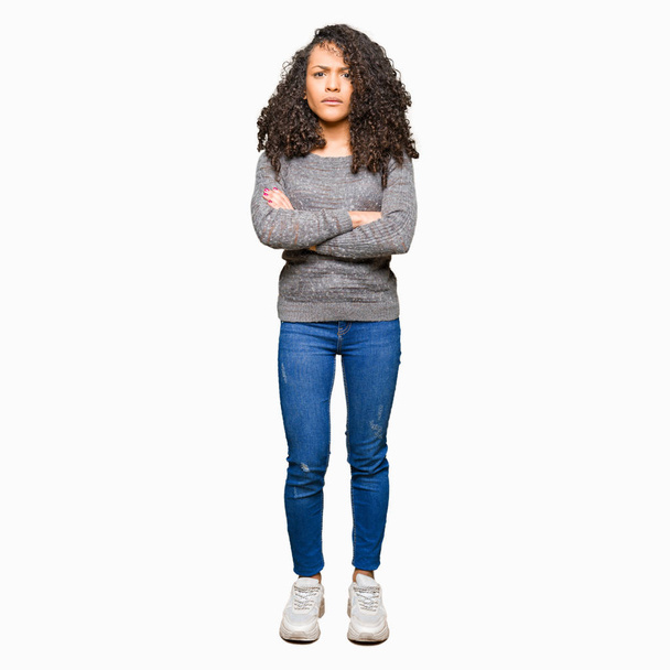 Young beautiful woman with curly hair wearing grey sweater skeptic and nervous, disapproving expression on face with crossed arms. Negative person. - 写真・画像