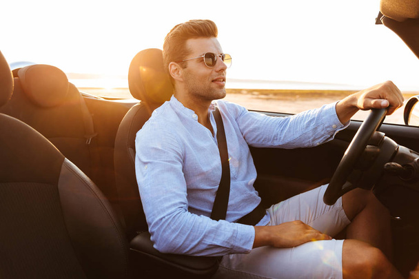 Photo of beautiful caucasian man driving convertible car by seas - 写真・画像