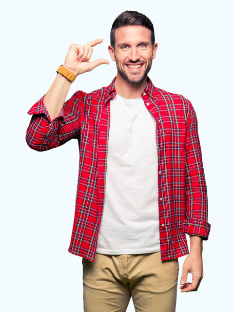 Hombre guapo con camisa casual sonriente y seguro de gesto con la mano haciendo signo de tamaño con los dedos mientras mira y la cámara. Concepto de medición
. - Foto, imagen