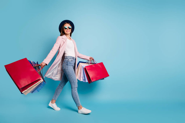 Full size photo of cute pretty cheerful lady in eyeglasses eyewear go shopping for bargains wear season cote denim jeans isolated over blue background - Foto, Imagem