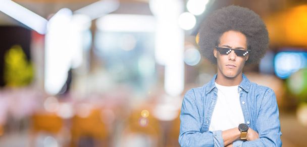 Young african american man with afro hair wearing thug life glasses skeptic and nervous, disapproving expression on face with crossed arms. Negative person. - Photo, Image