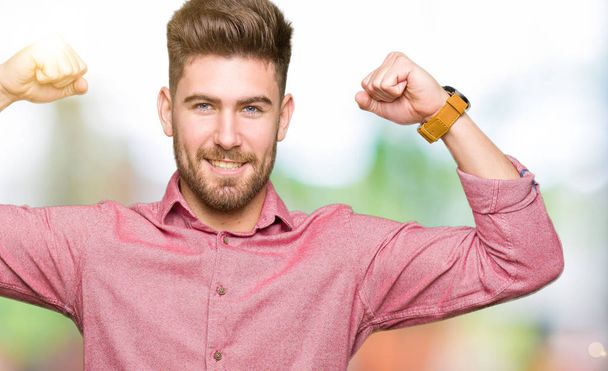 Mladý pohledný obchodní příležitostné muž ukazuje svaly paže s úsměvem hrdá. Fitness koncept. - Fotografie, Obrázek